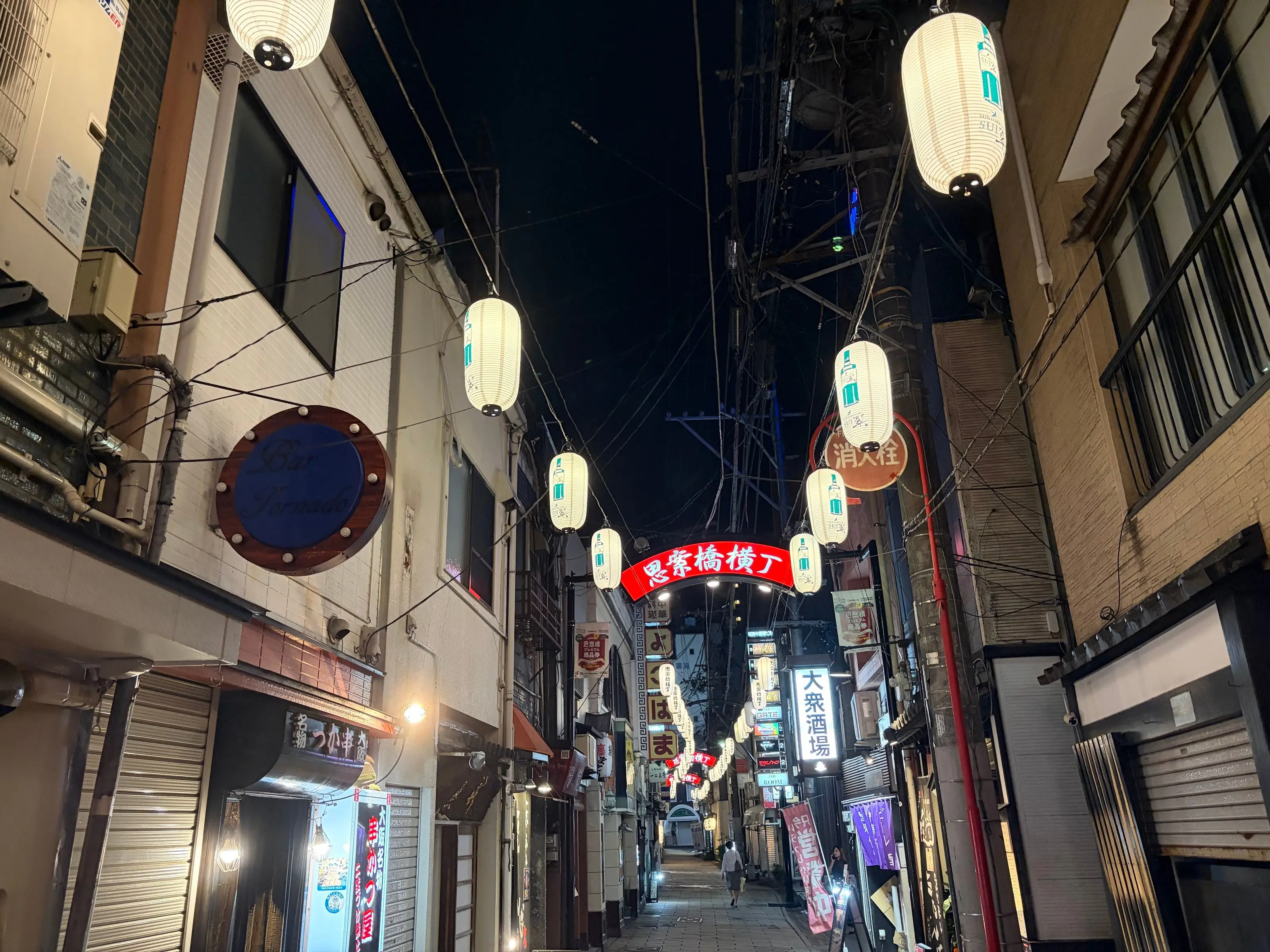 夜の横丁。電線に吊られた白い提灯が並び、奥に「思案橋横丁」の赤い看板